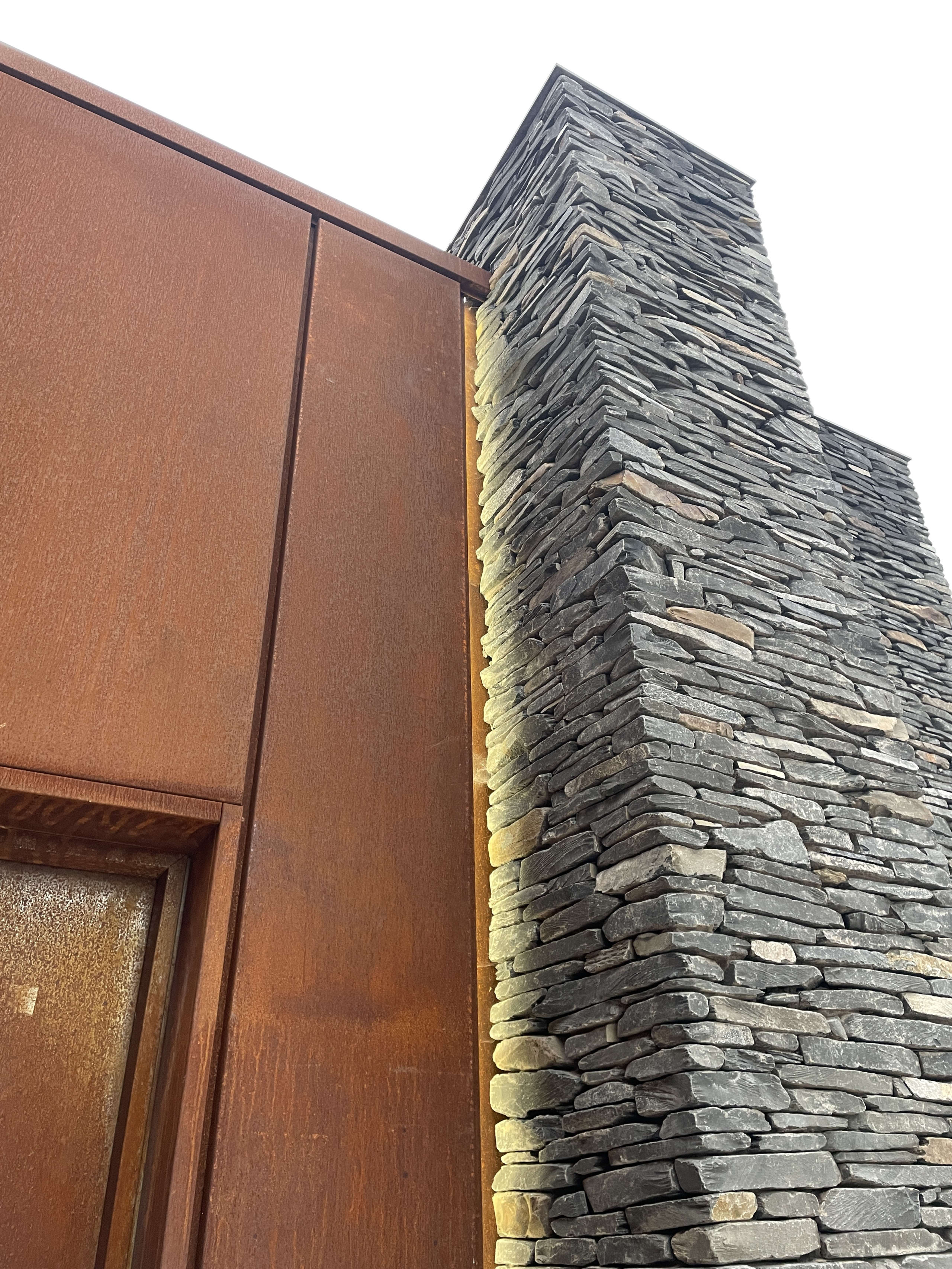 Corten steel cladding meets stacked slate stone chimney detail showcasing contrasting textures in contemporary architecture